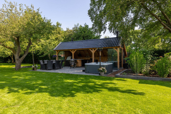 vooraanzicht-van-kapschuur-de-hoeve-met-douglas-constructie-zadeldak-en-open-zitgedeelte-in-een-groene-tuin