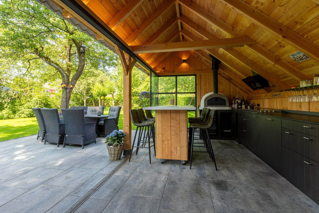 binnenzijde-van-kapschuur-de-hoeve-met-douglas-constructie-bar-tafel-buitenkeuken-en-zithoek-met-uitzicht-op-de-tuin