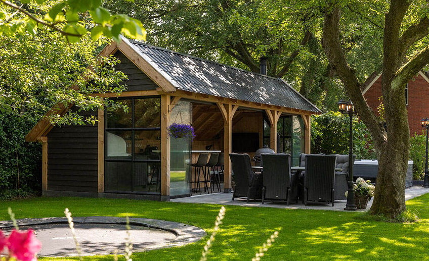 kapschuur-de-hoeve-met-douglas-constructie-zwarte-houten-wanden-zadeldak-steellook-ramen-glazen-schuifwand-en-open-zitgedeelte-in-een-groene-tuin