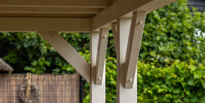 detail-van-witte-houten-veranda-constructie-met-staanders-schoren-en-dakbalken