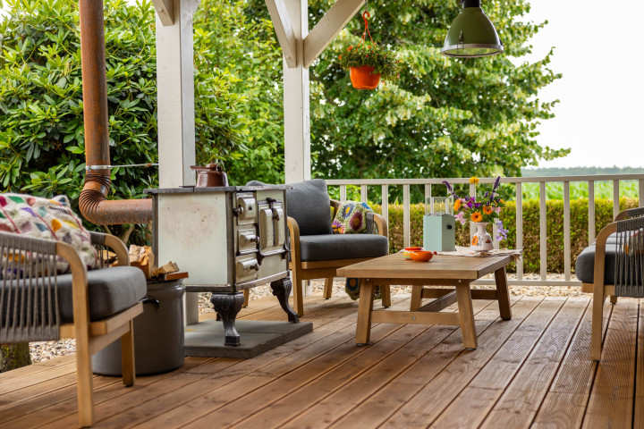 sfeervolle-veranda-met-houten-vlondervloer-zitmeubels-salontafel-en-houtkachel-voor-een-gezellige-buitenruimte