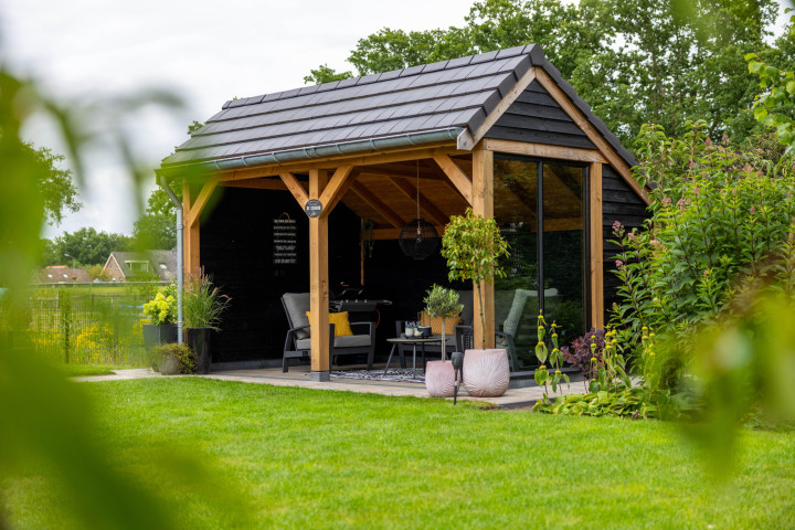 landelijke-houten-kapschuur-met-open-overkapping-in-een-groene-tuin-met-douglas-houten-constructie-zwarte-potdeksel-planken-en-donkere-dakpannen