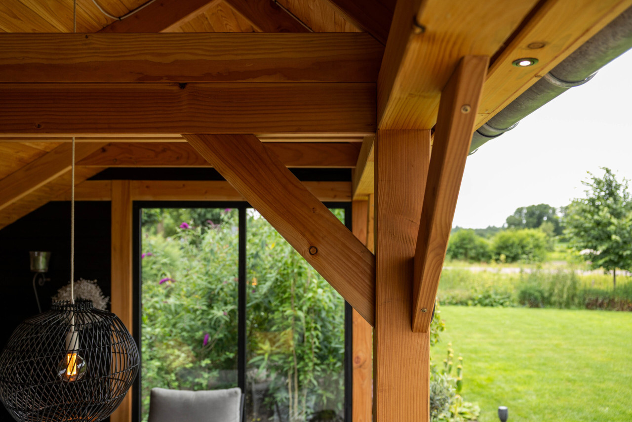 detail-van-douglas-houten-kapschuur-constructie-met-schore-balken-en-overstek-met-uitzicht-op-een-groene-tuin