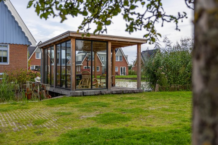 zijaanzicht-van-lichte-en-open-tuinkamer-overkapping-siena-met-glazen-wanden-op-vlonder-aan-het-water-in-de-tuin