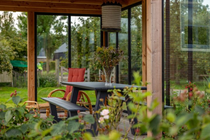 detail-van-de-binnenkant-van-tuinkamer-overkapping-siena-met-zithoek-glazen-wanden-en-bloemen-en-planten-op-de-vlonder-aan-het-water