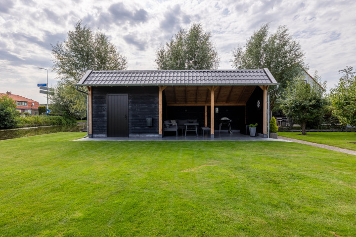 vooraanzicht-van-kapschuur-de-heerd-met-douglas-constructie-zwarte-houten-wanden-open-zitgedeelte-en-berging-in-de-tuin