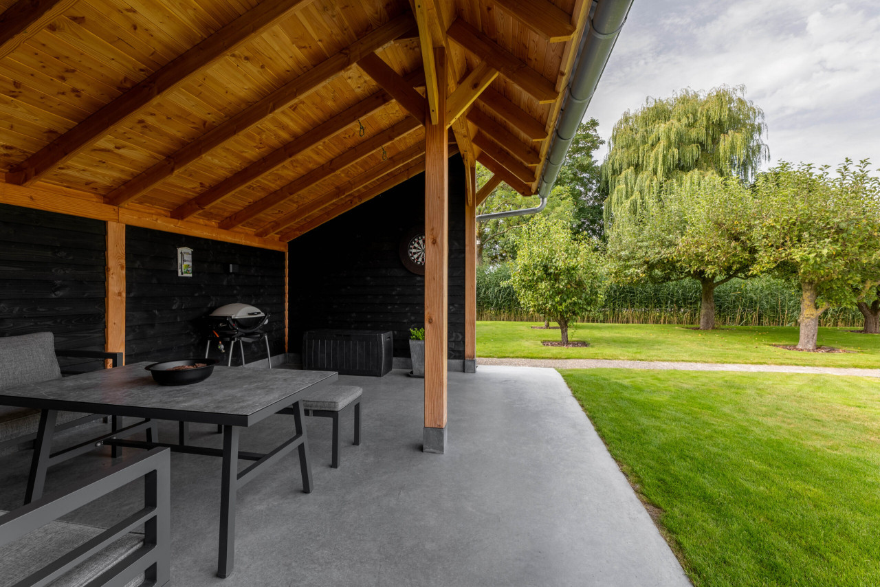open-zitgedeelte-van-kapschuur-de-heerd-met-douglas-constructie-betonvloer-zithoek-en-uitzicht-op-de-tuin