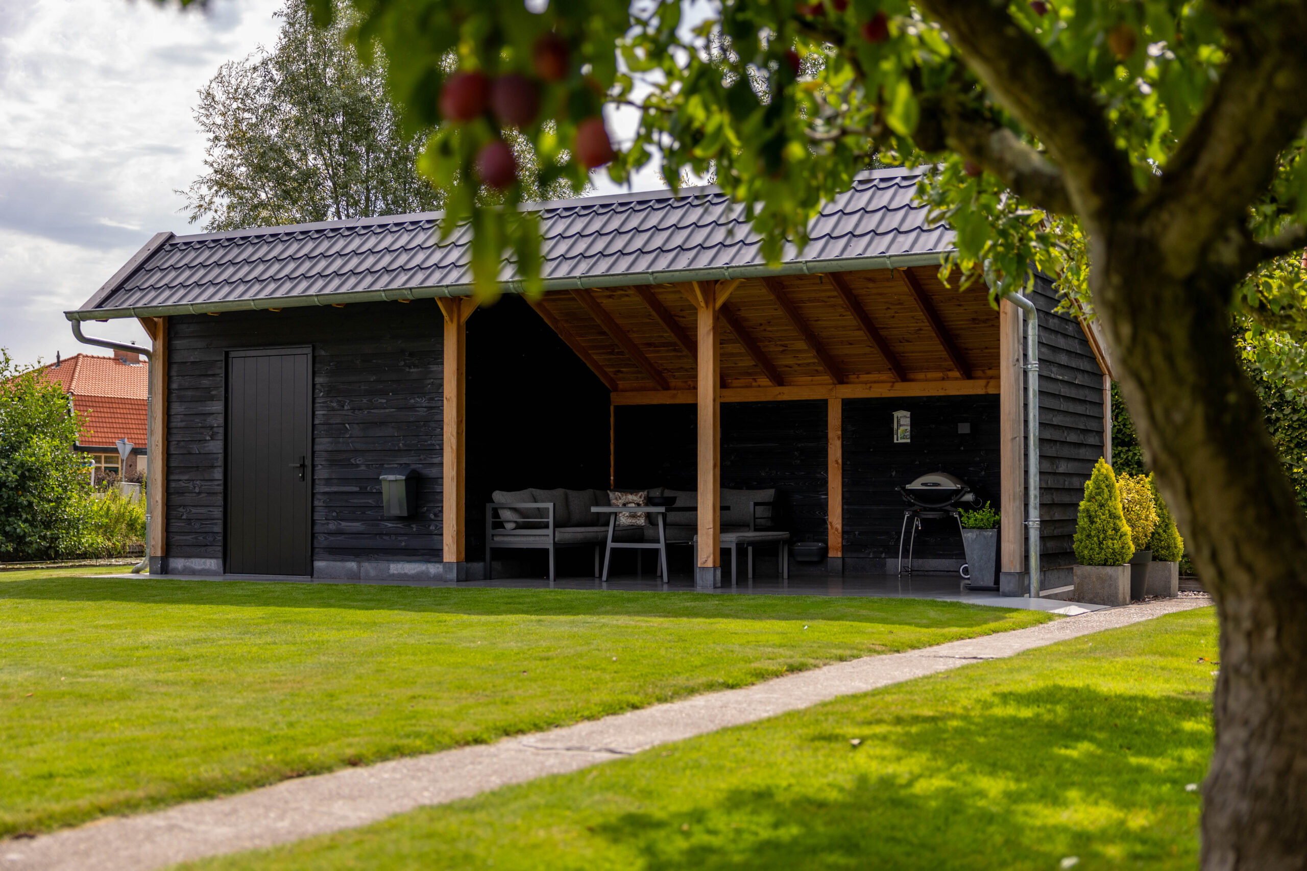 kapschuur-de-heerd-met-douglas-constructie-zwarte-houten-wanden-donker-dak-open-zitgedeelte-en-berging-in-de-tuin