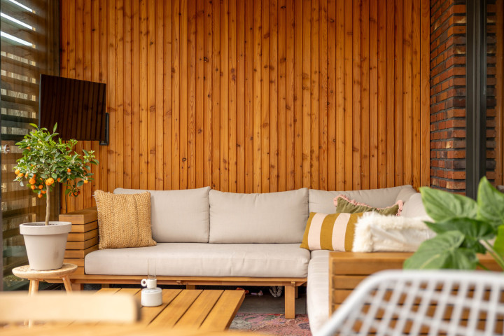 detail-van-loungehoek-in-aanbouwveranda-modena-met-thermisch-vuren-wand-en-houten-zitbank