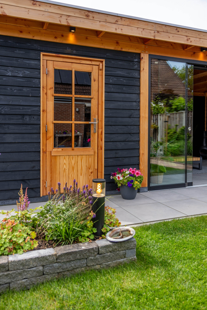 detail-van-modern-tuinhuis-met-zwarte-houten-gevel-houten-deur-en-glazen-schuifpui