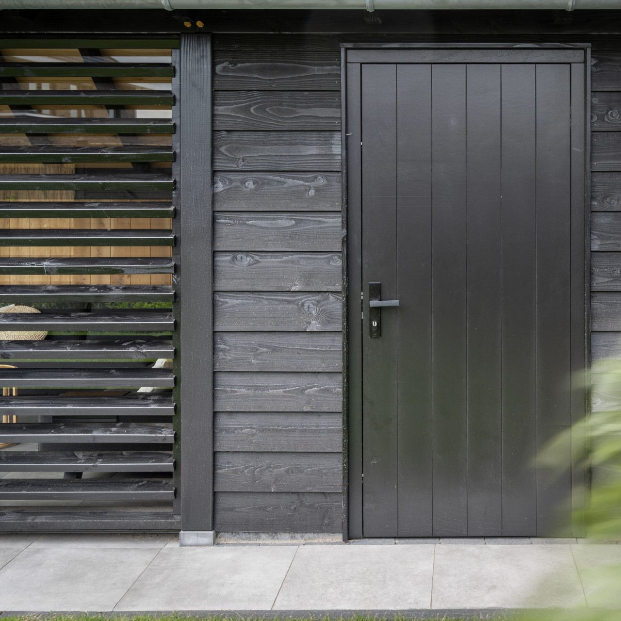 detail-van-louvre-en-hardhouten-plaatdeur-bij-kapschuur-de-hoeve-xl-met-wanden-van-douglas-potdekselplanken-zwart
