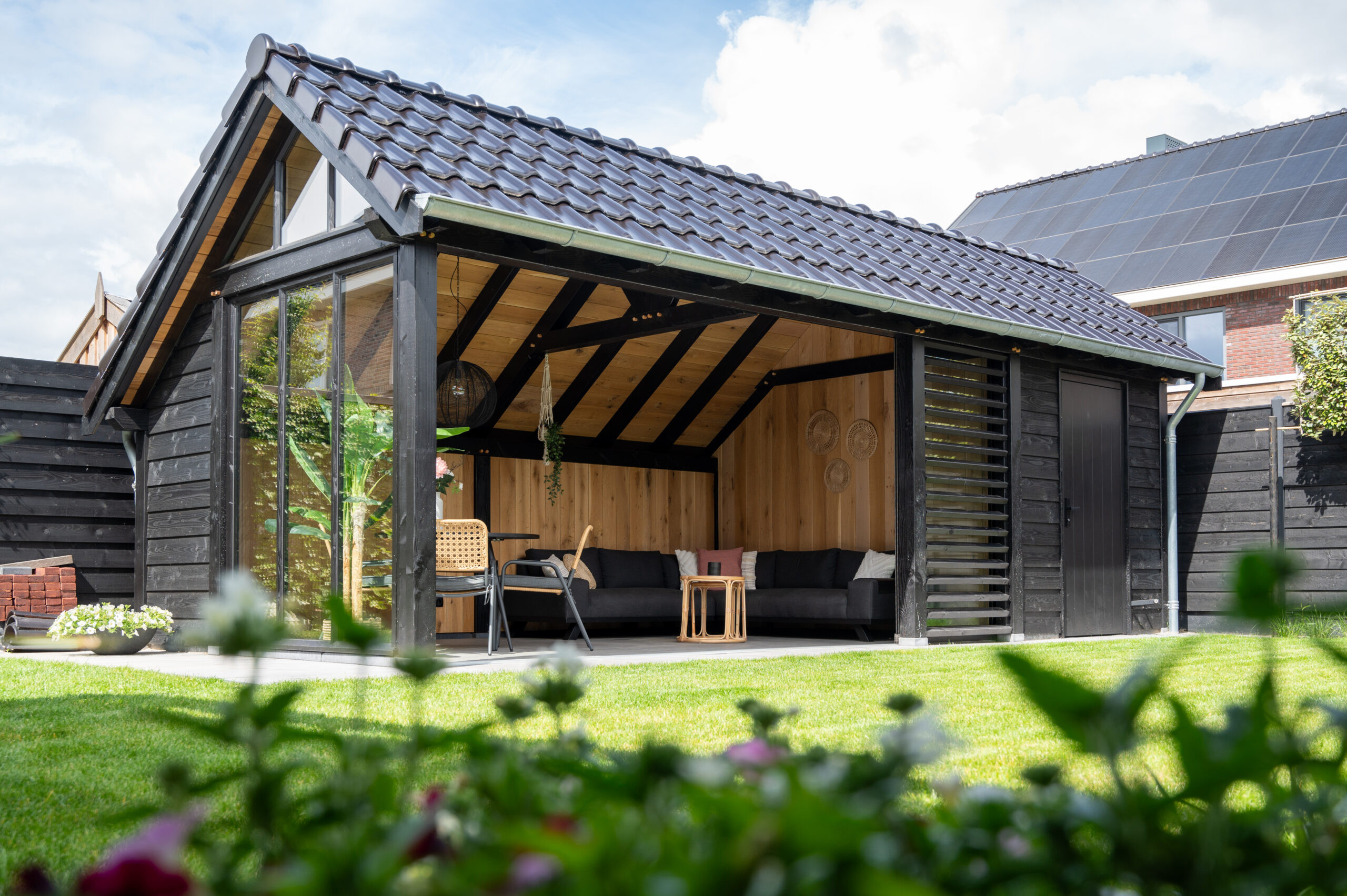 kapschuur-de-hoeve-xl-met-douglas-constructie-wanden-van-douglas-potdekselplanken-zwart-en-eiken-sponningsplanken-louvre-glazen-schuifwand-hardhouten-plaatdeur-steellook-raam-en-zinken-dakgoot-in-de-tuin