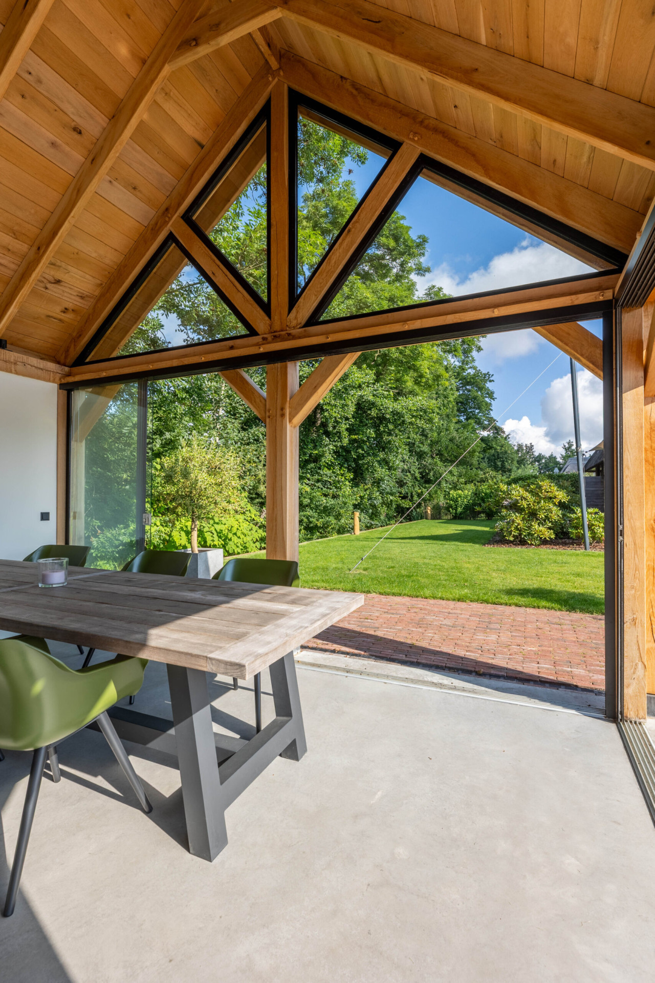 binnenaanzicht-van-zadeldak-eiken-met-eiken-constructie-glazen-schuifwand-steellook-topgevel-en-tafel-met-uitzicht-op-de-tuin