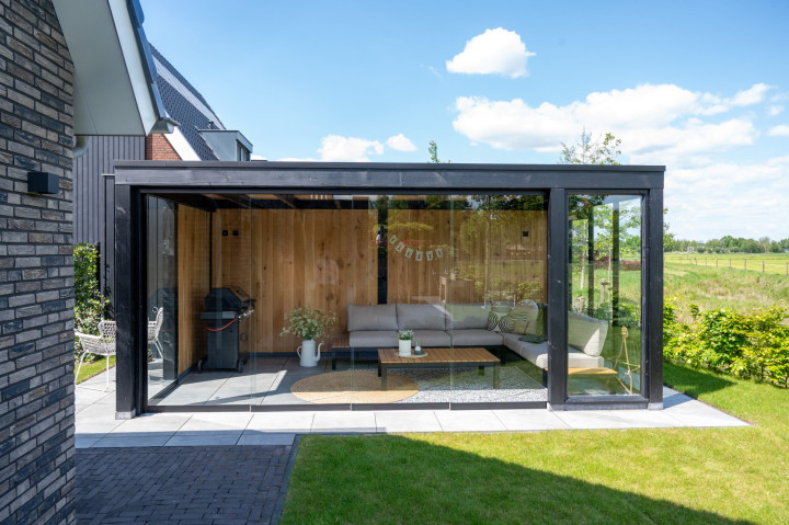 vooraanzicht-van-overkapping-palermo-met-zwarte-douglas-constructie-eiken-sponningsplanken-steellook-raam-en-glazen-schuifwanden-in-de-tuin