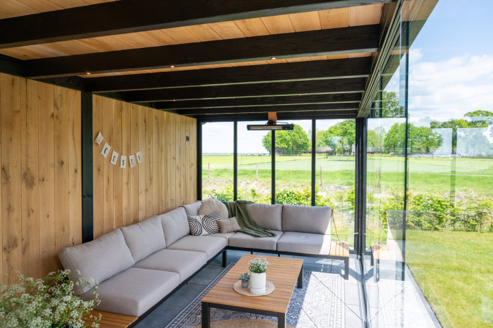 binnenaanzicht-van-overkapping-palermo-met-zwarte-douglas-constructie-wanden-van-eiken-sponningsplanken-glazen-schuifwanden-en-loungehoek-met-uitzicht-op-de-tuin